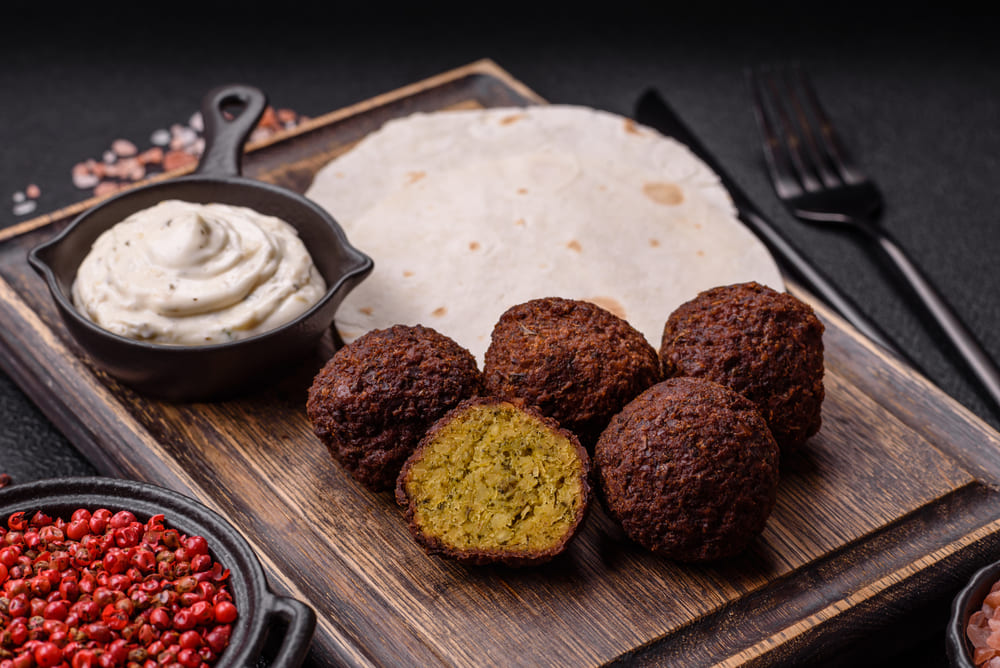 Zdjęcie chrupiących kotlecików falafel na talerzu. Falafel to wyśmienite źródło białka w diecie wegańskiej, wzbogacone aromatycznymi przyprawami. Doskonale wpisuje się w ofertę cateringu dietetycznego, zapewniając sycące i smakowite dania.